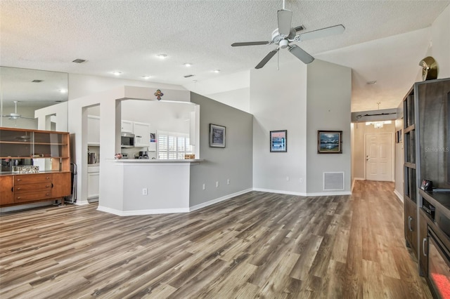 unfurnished living room with a ceiling fan, wood finished floors, lofted ceiling, a textured ceiling, and baseboards