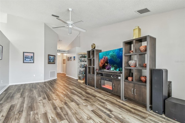 living area with lofted ceiling, wood finished floors, ceiling fan, a textured ceiling, and baseboards