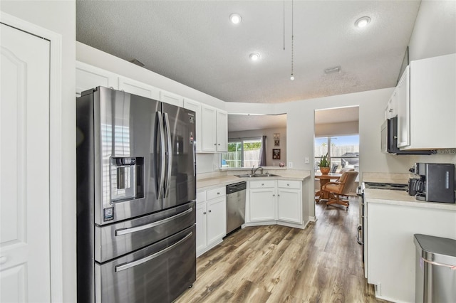 kitchen with appliances with stainless steel finishes, a sink, light countertops, white cabinetry, and light wood-style flooring