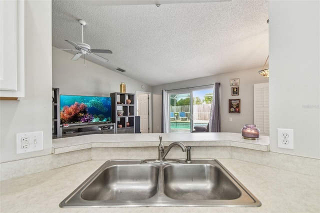 kitchen with a sink, a textured ceiling, vaulted ceiling, ceiling fan, and light countertops