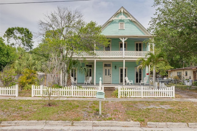 victorian home featuring covered porch, a balcony, and a fenced front yard