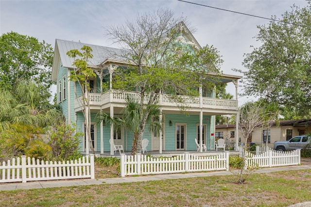 victorian-style house featuring a balcony, a porch, a fenced front yard, and metal roof