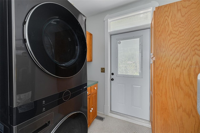 washroom featuring stacked washing machine and dryer, cabinet space, and light tile patterned floors
