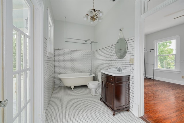 full bath with a freestanding tub, vanity, a chandelier, tile patterned flooring, and tile walls