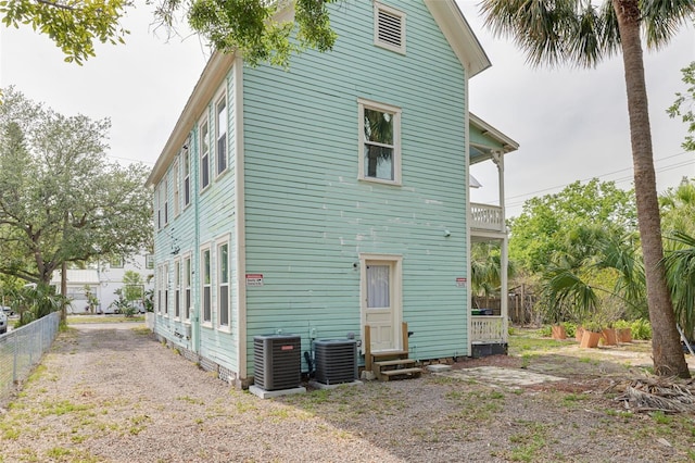 rear view of house with central air condition unit, entry steps, a balcony, and fence