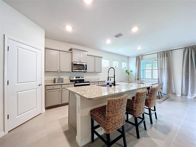 kitchen featuring appliances with stainless steel finishes, gray cabinets, a sink, a breakfast bar area, and a kitchen island with sink