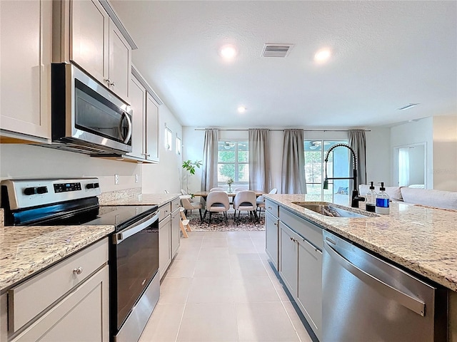 kitchen featuring appliances with stainless steel finishes, a sink, light stone countertops, recessed lighting, and gray cabinetry