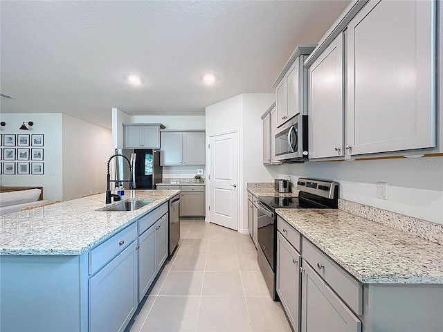 kitchen with appliances with stainless steel finishes, a sink, gray cabinets, a center island with sink, and light tile patterned flooring