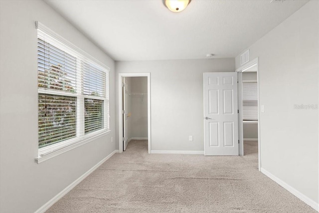 unfurnished bedroom with carpet flooring, baseboards, a spacious closet, and a closet
