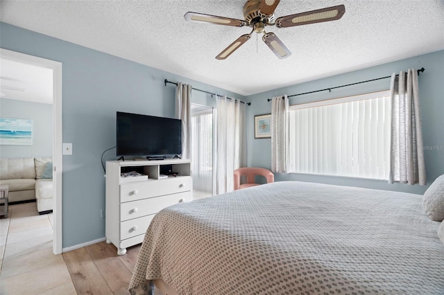 bedroom featuring light wood-style flooring, baseboards, a textured ceiling, and a ceiling fan