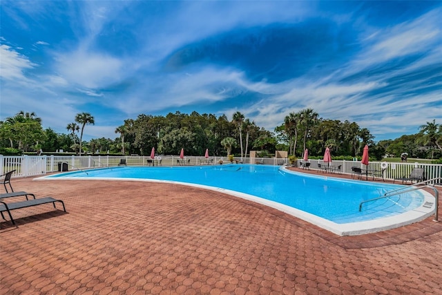 community pool featuring fence, view of scattered trees, and a patio