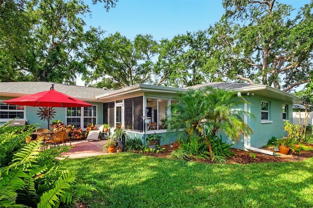 rear view of property with a sunroom, a lawn, stucco siding, and a patio