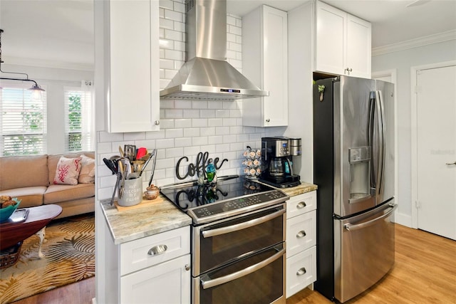 kitchen featuring stainless steel appliances, wall chimney exhaust hood, ornamental molding, backsplash, and white cabinets