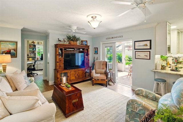 living room featuring ceiling fan, light wood finished floors, crown molding, a desk, and baseboards