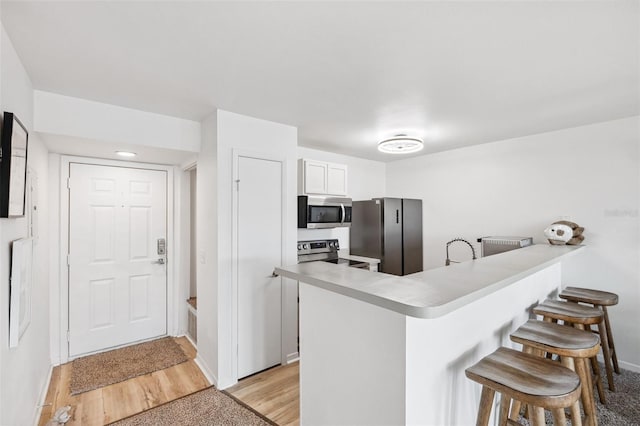5712 Biscayne Ct Unit 103, New Port Richey, FL 34652 - kitchen with appliances with stainless steel finishes, a breakfast bar area, a peninsula, baseboards, and white cabinetry