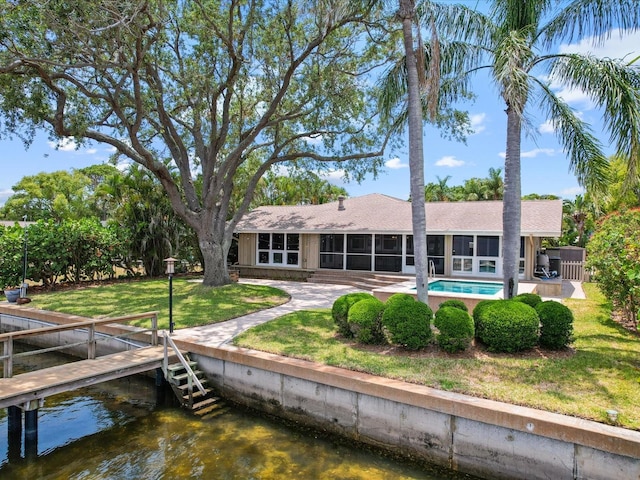 rear view of house featuring a sunroom, a water view, a shingled roof, and a lawn