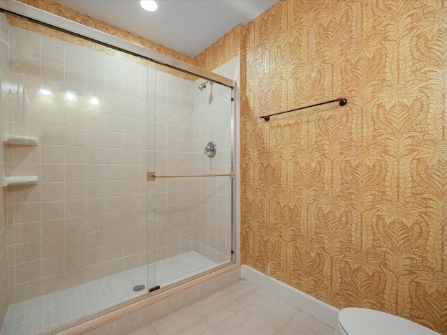 bathroom with wallpapered walls, baseboards, toilet, a shower stall, and tile patterned floors