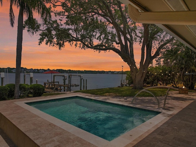 pool at dusk featuring a water view, a boat dock, and boat lift