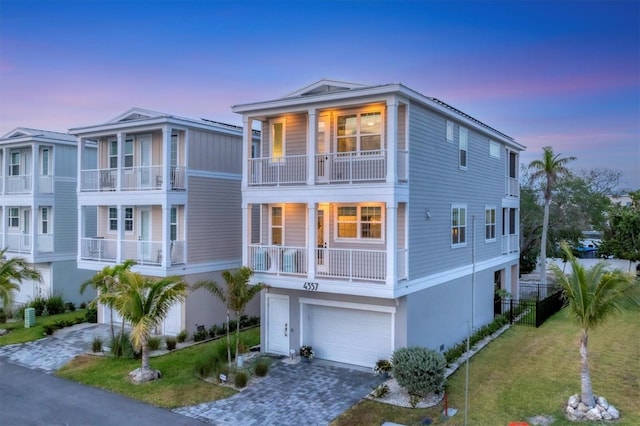 coastal inspired home with a garage, driveway, a balcony, and stucco siding