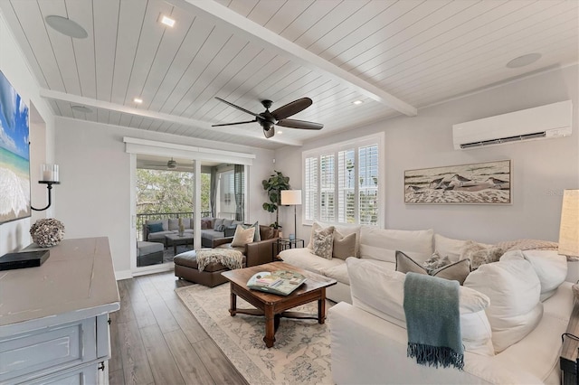 living room with a wall unit AC, healthy amount of natural light, wood finished floors, beam ceiling, and ceiling fan