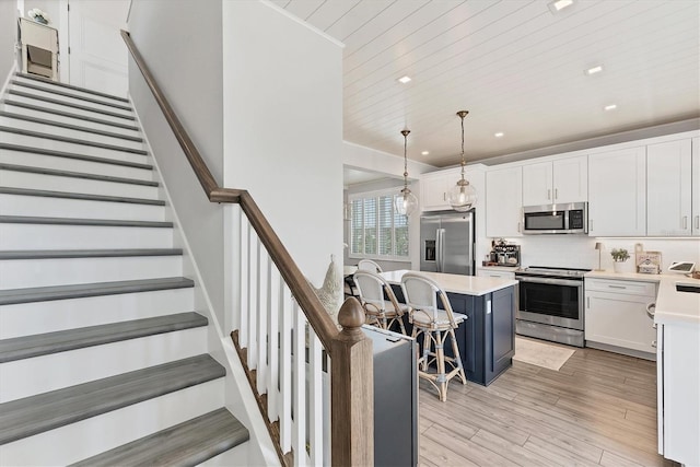 kitchen featuring stainless steel appliances, a kitchen breakfast bar, light countertops, white cabinets, and tasteful backsplash
