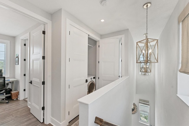 hall featuring a chandelier, light wood finished floors, baseboards, and washer / clothes dryer