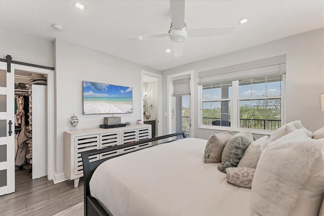 bedroom featuring wood finished floors, a walk in closet, recessed lighting, a ceiling fan, and a barn door