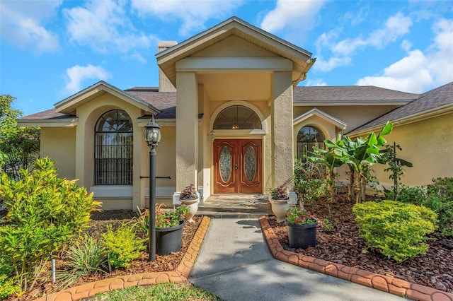 entrance to property featuring stucco siding and a shingled roof
