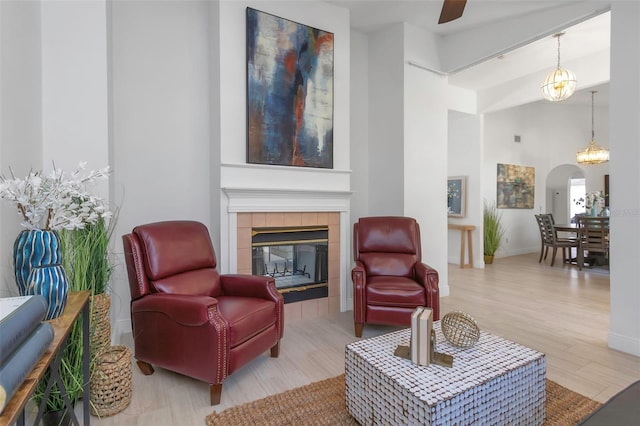 living area with wood finished floors, a tiled fireplace, arched walkways, ceiling fan, and baseboards