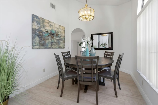 dining room featuring arched walkways, a high ceiling, a chandelier, and baseboards