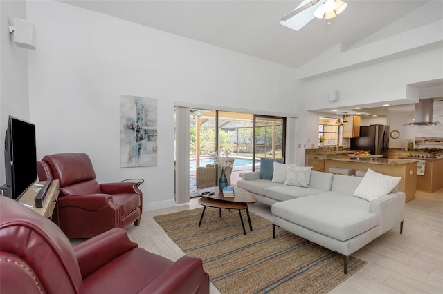 living room featuring ceiling fan, high vaulted ceiling, baseboards, and light wood-style flooring
