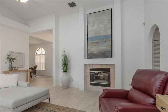 living area featuring arched walkways, a tiled fireplace, a ceiling fan, wood finished floors, and baseboards