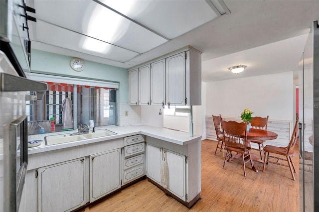 3621 Beacon Square Dr, Holiday, FL 34691 - kitchen featuring light wood-type flooring, light countertops, a sink, decorative backsplash, and a peninsula