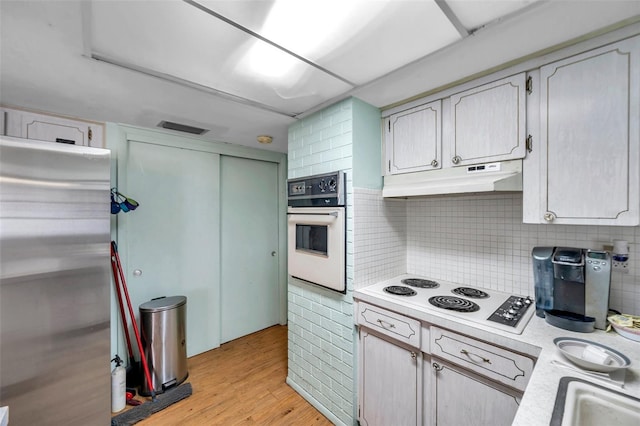 3621 Beacon Square Dr, Holiday, FL 34691 - kitchen featuring white appliances, under cabinet range hood, light countertops, light wood-style flooring, and backsplash