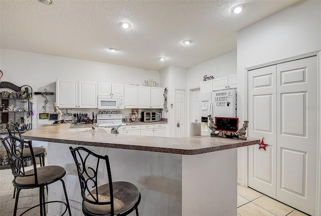 14985 Alan Ct, Largo, FL 33771 - kitchen featuring white appliances, a breakfast bar, a textured ceiling, white cabinets, and light tile patterned floors