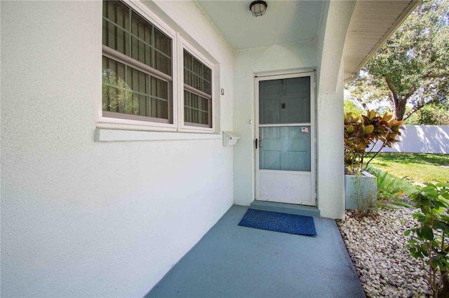 view of exterior entry with stucco siding and fence