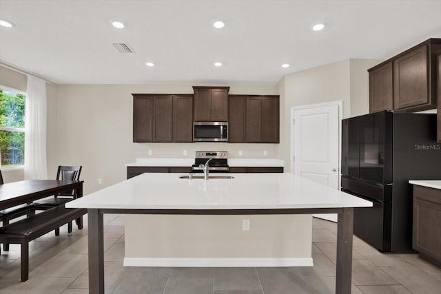 10379 Bridgegate Heights Loop, San Antonio, FL 33576 - kitchen featuring appliances with stainless steel finishes, an island with sink, dark brown cabinetry, light countertops, and recessed lighting