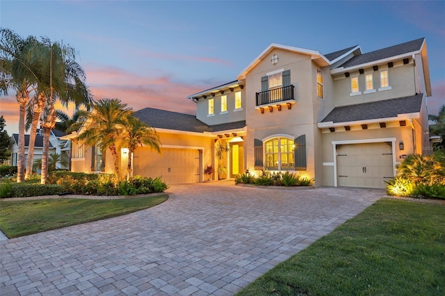 mediterranean / spanish home featuring a balcony, decorative driveway, stucco siding, and a front lawn