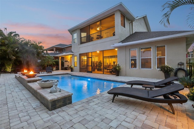 back of house at dusk featuring a balcony, a fire pit, stucco siding, and a patio area