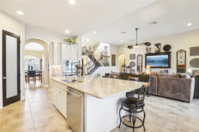 kitchen with arched walkways, stainless steel appliances, a sink, light stone countertops, and a kitchen island with sink