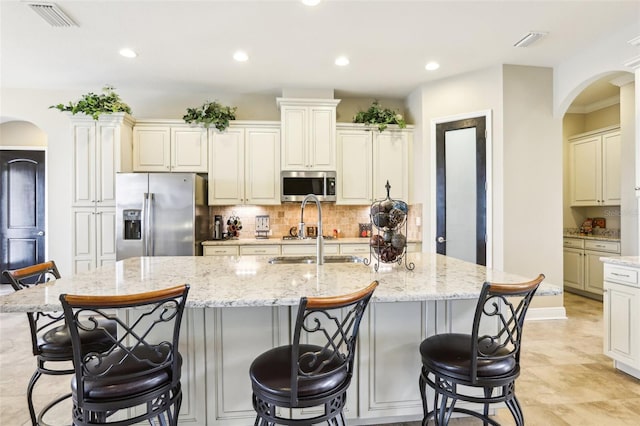kitchen with appliances with stainless steel finishes, arched walkways, a sink, light stone counters, and recessed lighting