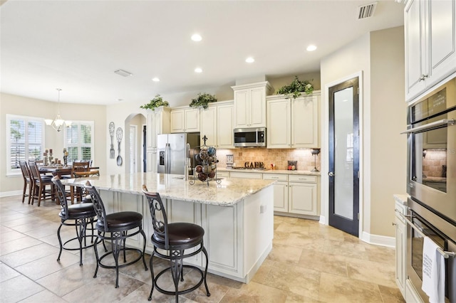 kitchen with appliances with stainless steel finishes, an island with sink, a chandelier, tasteful backsplash, and recessed lighting