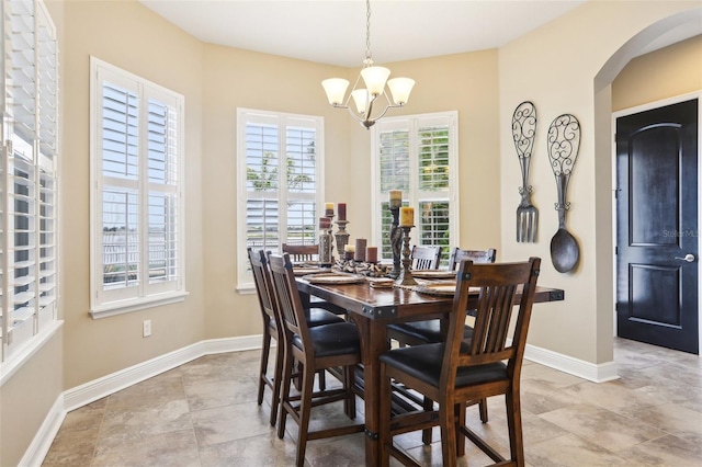 dining area featuring a chandelier, arched walkways, and baseboards