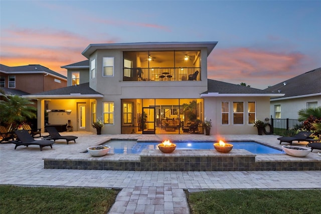 back of house at dusk with a fire pit, a balcony, stucco siding, and a jacuzzi