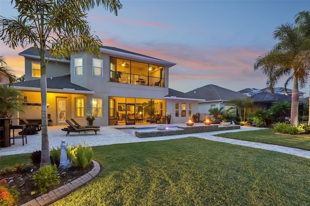 back of property at dusk with a balcony, a lawn, a patio area, an outdoor hot tub, and stucco siding