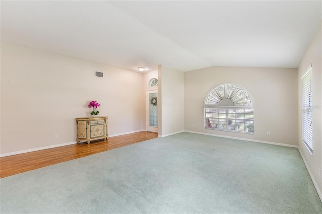 spare room featuring carpet flooring, baseboards, and lofted ceiling
