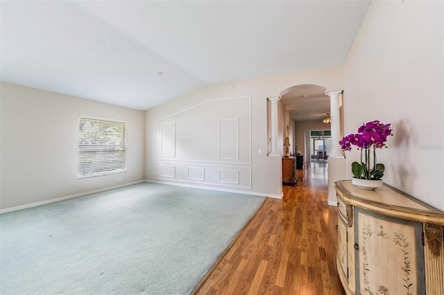 foyer entrance featuring decorative columns, arched walkways, wood finished floors, baseboards, and lofted ceiling