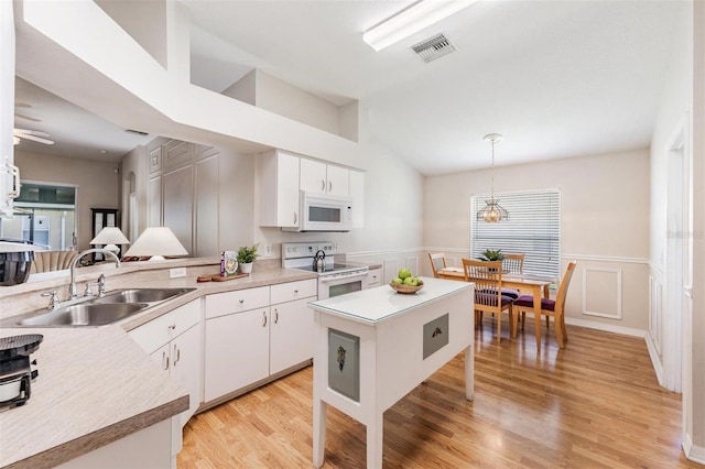 kitchen featuring white appliances, a sink, lofted ceiling, hanging light fixtures, and white cabinetry