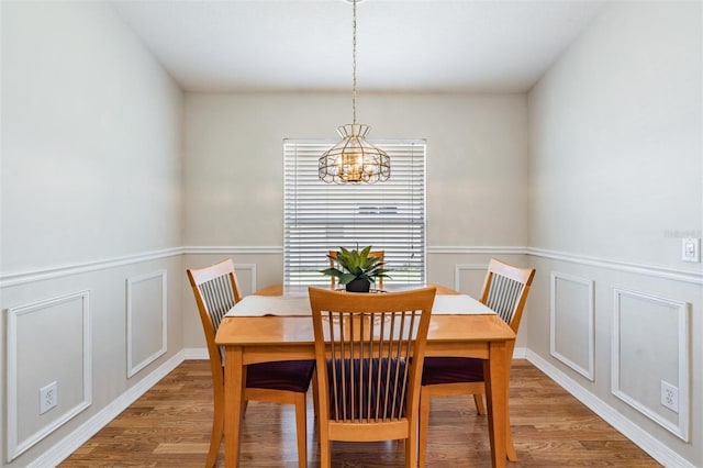 dining space with light wood finished floors, a decorative wall, wainscoting, and a chandelier