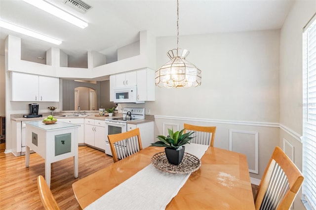 dining space featuring arched walkways, a chandelier, light wood-style flooring, a decorative wall, and wainscoting